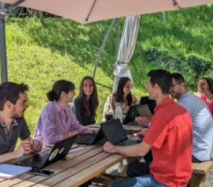 personnes autour d'une table dehors en été en train de travailler sur leur ordinateur